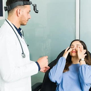 Kobieta leży na fotelu zabiegowym i dotyka swojego nosa, obok stoi lekarz