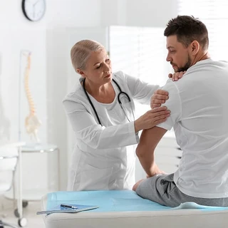 Lekarka bada ramię pacjenta w gabinecie.